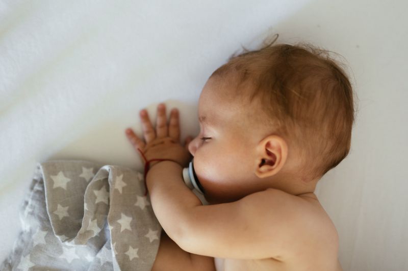 baby sleeping with a pacifier in their mouth with a gray blanket that has stars